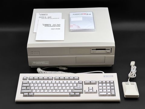 Amiga 2000 desktop case straight-on with its keyboard and mouse in front, and A2091-40 and A2630 accelerator manuals plus an AmigaOS 3.x disc case lying on top of the case