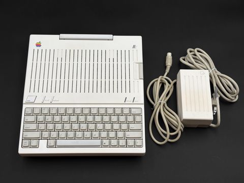 Apple IIc from above on the dark backdrop with its external power supply and coiled cord laid beside it