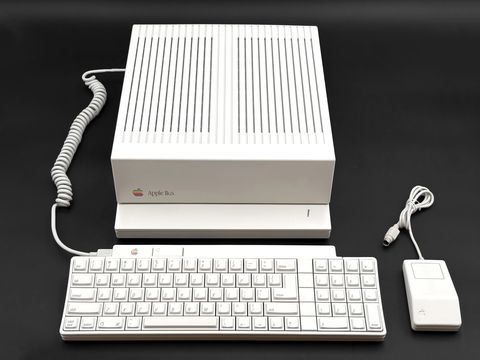 An Apple IIgs system unit stands above its keyboard with a coiled cable, with a one-button Desktop Bus mouse to the right, all shot from above