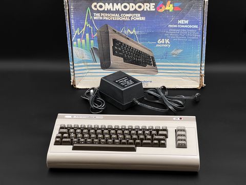 Commodore 64 breadbin computer in front of its original Commodore 64 retail box with the power supply laid between them