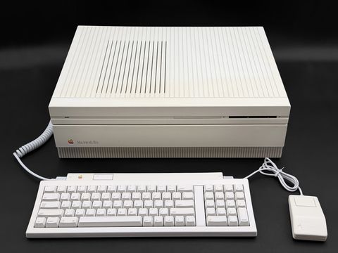 Front three-quarter-from-above view of the Macintosh IIfx desktop case with its coiled keyboard cable, an Apple Keyboard II (with keypad) and a one-button ADB mouse laid out in front (no monitor)